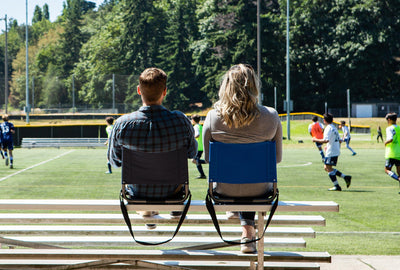 A couple sits and watches a soccer game from the bleachers